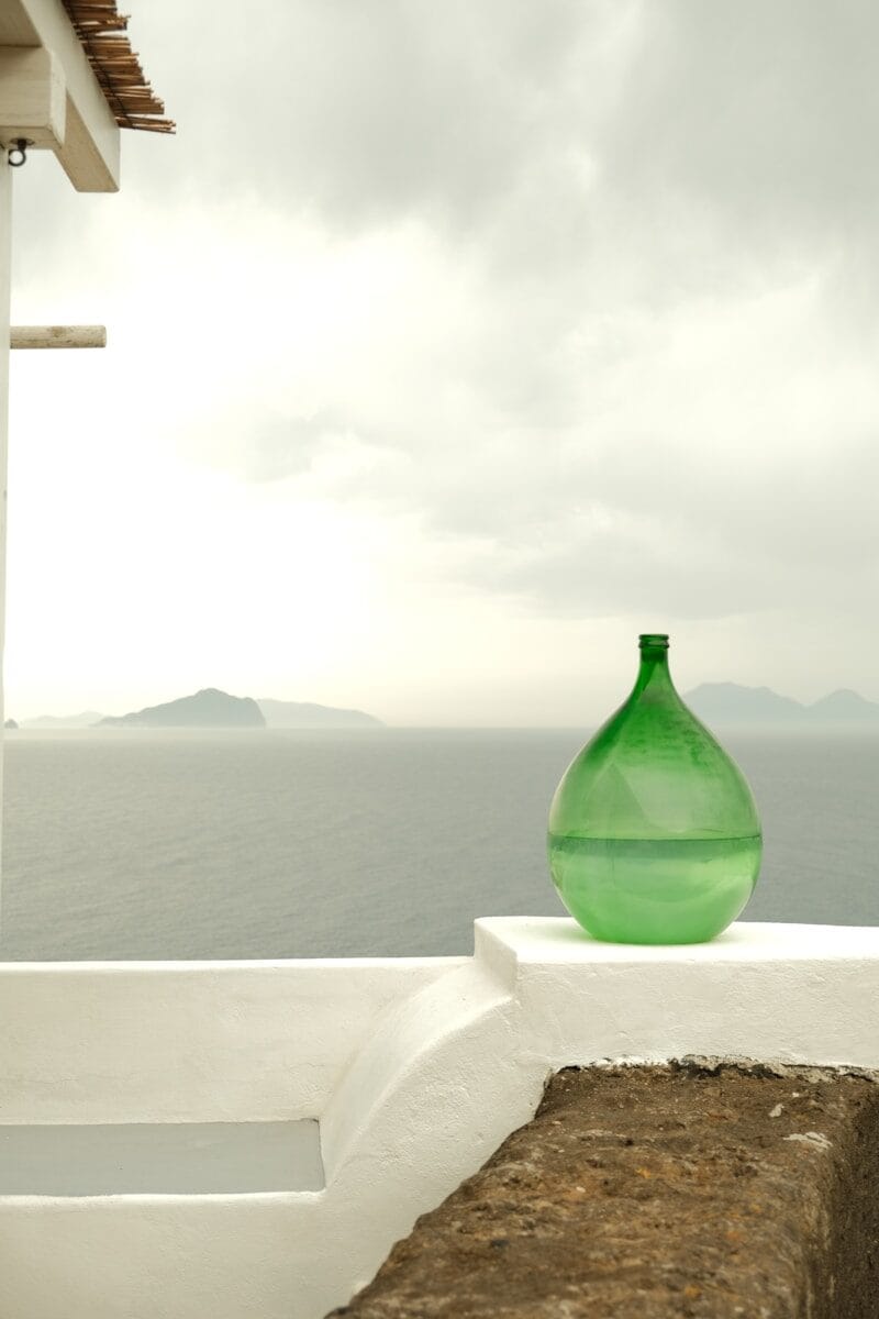 Green vase sits by the sea under a cloudy sky.